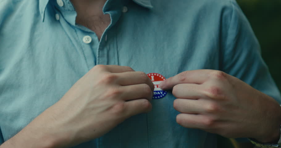 Young man smiling with an ‘I Voted’ sticker and pin 