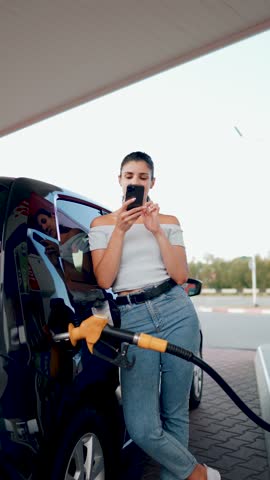 A woman fills a car with fuel at a gas station. Gas station service. Refueling concept. Vertical video 4k