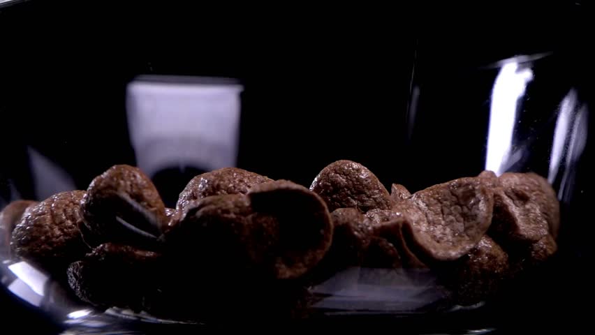 Chocolate flakes or chocolate crunch cereal for breakfast. Pouring milk into chocolate cereals in glass bowl. pouring milk into bowl with chocolate cereals.