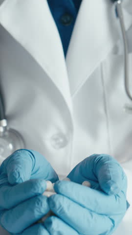 In a symbolic image, a healthcare worker wearing blue gloves is holding white capsules, representing medication and pharmaceuticals. Keywords include antibiotics, pills, prescription