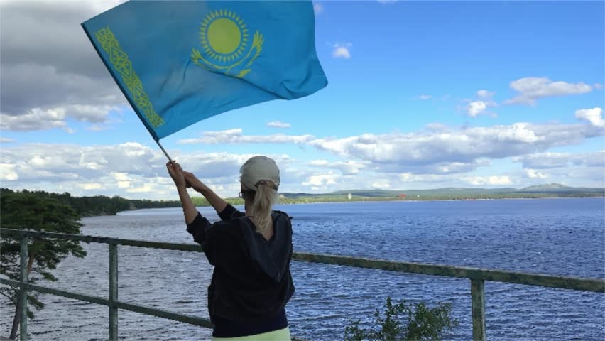 Young woman traveling in the Kazakhstan. She is standing by back and holding the blue of Kazakhstan Republic. Borovoe lake view