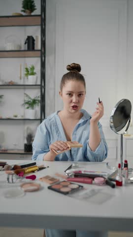 Beautiful woman doing makeup in morning, talking with followers in social media, vertical video. Portrait of beauty blogger showing how to makeup, demonstrating trendy eyeshadows, cosmetics products