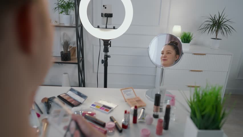 Cheerful makeup artist filing video tutorial for blog in social media in studio. Influencer advertising cosmetics brand and showing how to makeup, live streaming and talk for followers, online work