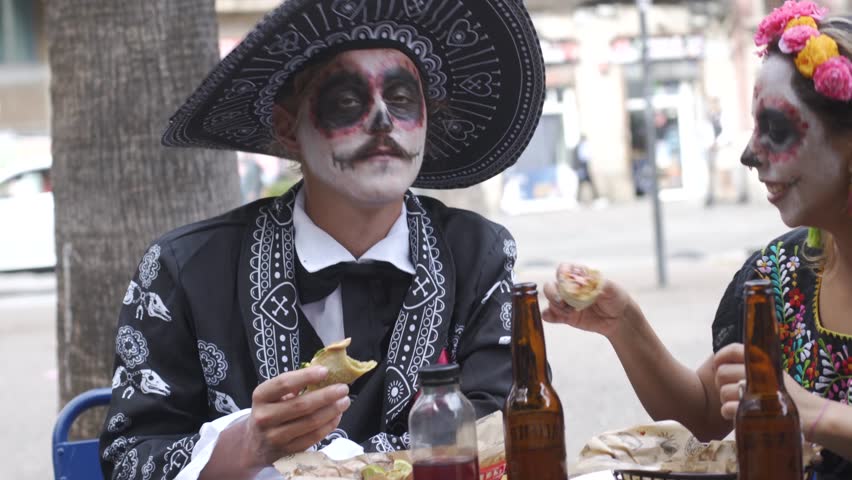 Couple Dressed as Mexican Catrin and Catrina Enjoying Tacos