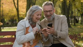 Elderly couple Caucasian mature woman man family using mobile phone on bench in park outdoors cheerful spouses read news laughing make order with smartphone female male old age use technology in city - Powered by Shutterstock - Get 15% off with code: PIKWIZARD15