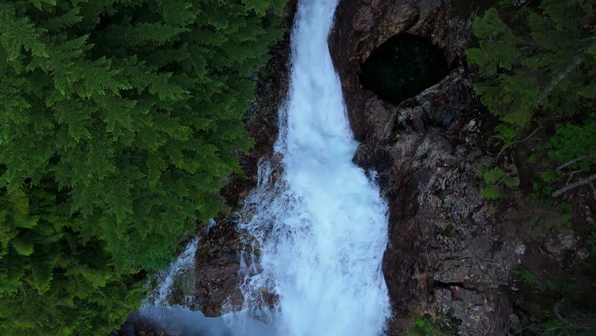 Scenic fly over shot above flowing waterfall and Evergreen forest in the Pacific Northwest