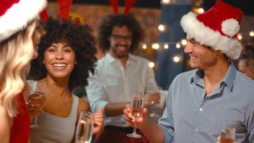Multi-cultural group of friends wearing santa hats celebrating making a toast with champagne enjoying Christmas party night out in bar or club - shot in slow motion - Powered by Shutterstock - Get 15% off with code: PIKWIZARD15