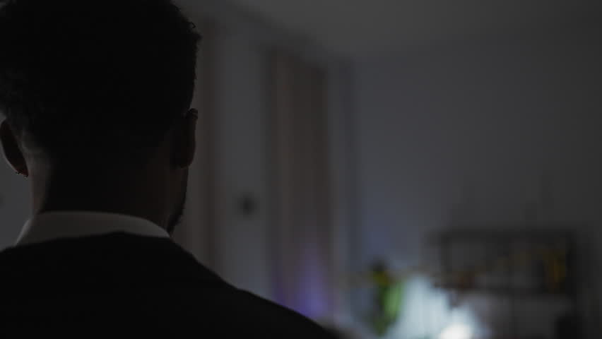 Silhouetted man in suit indoor mysterious darkened room illuminated with subtle blue light contemplating.