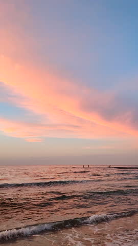 Beautiful seascape during red orange sunrise. Red orange yellow clouds on blue sky reflected on the surface of the sea on the sandy shore of the sea coast at dawn. Nature. Natural background. Vertical