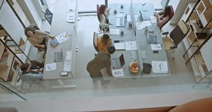 Overhead view of a group of people engaging in discussions and strategizing in a well-lit, open-plan office setting. Team members are seen at separate desks, collaborating and working on laptops. - Powered by Shutterstock - Get 15% off with code: PIKWIZARD15