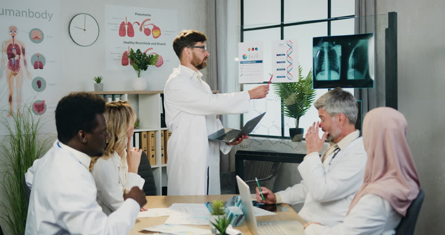 Handsome confident high-skilled bearded doctor explaining dna structure for attantive motivated qualified diverse colleagues during joint briefing in clinic office