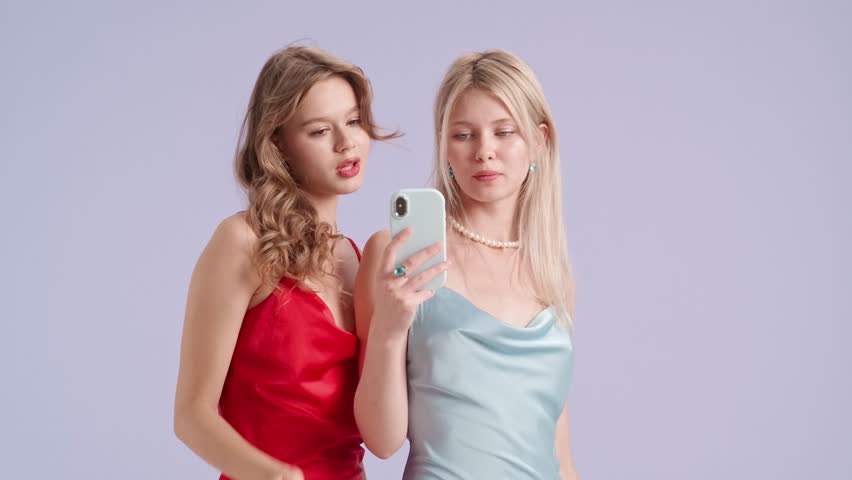 Young stylish women models holding smartphone watching social media scrolling, isolated on purple background. Fashion and youth beauty concept.