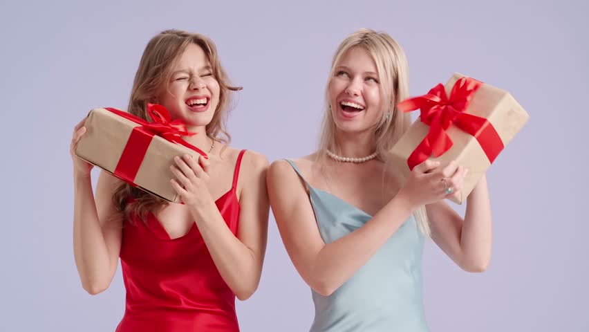 Young stylish women models holding gift boxes, shaking presents and guessing, isolated on purple background. Fashion and youth beauty concept.