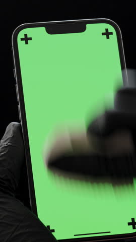 Vertical video. Hands in Black Nitrile Gloves Wiping the Screen of a Smartphone with a Cloth, Chroma Key, Isolated on a Black Background.