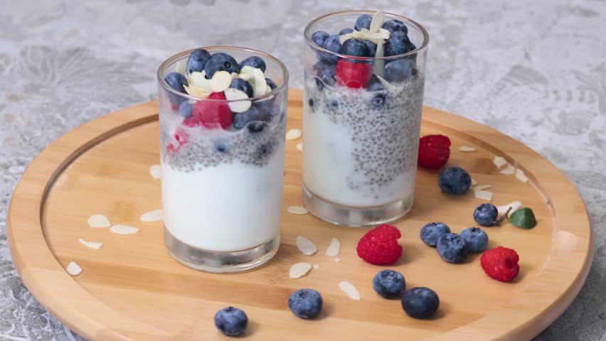 Rotating glasses of berry pudding and chia on wooden base. Raspberries and blueberries. Healthy food and nutrition. 