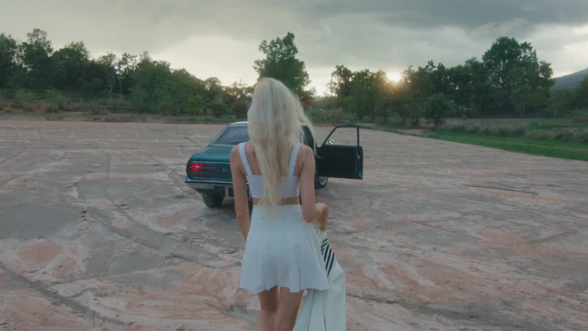 A woman is walking leisurely towards a car, enjoying the beautiful outdoor scenery