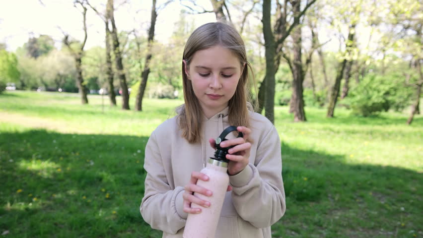 Adorable Small Schoolgirl Sipping Water From A Bottle In The Park