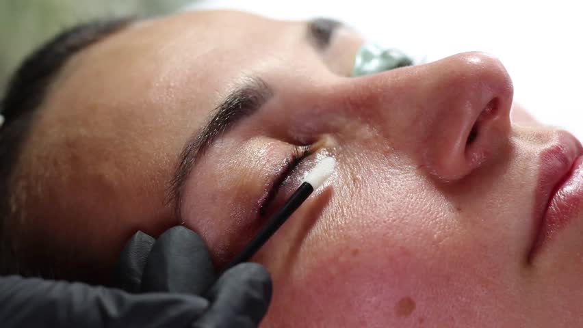 Close-up of a professional applying tint to a woman's eyelashes during a beauty treatment. The process enhances the color and definition of the lashes for a more polished look.