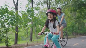 Asian young mother and daughter riding bicycle outdoors in the garden. Happy family, attractive mommy in sportswear feeling happy and relax, exercise in public park with adorable kid girl for health. - Powered by Shutterstock - Get 15% off with code: PIKWIZARD15
