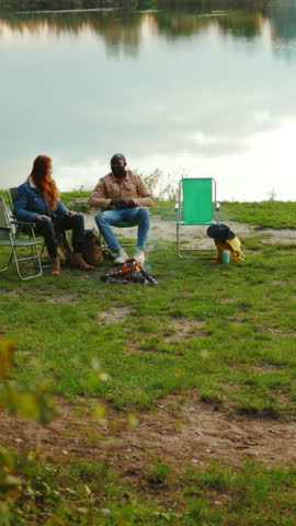 Near lake hipster friends met eath other sitting near lake. Four young people hug smiling with dog. Vacation tourism adventure outdoors. Close up. Slow motion
