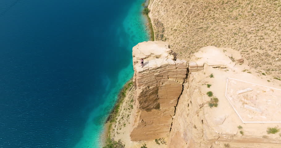 Man Standing On Top Of Cliff Overlooking Blue Lake At Band-e Amir National Park In Bamyan, Afghanistan. aerial orbiting shot