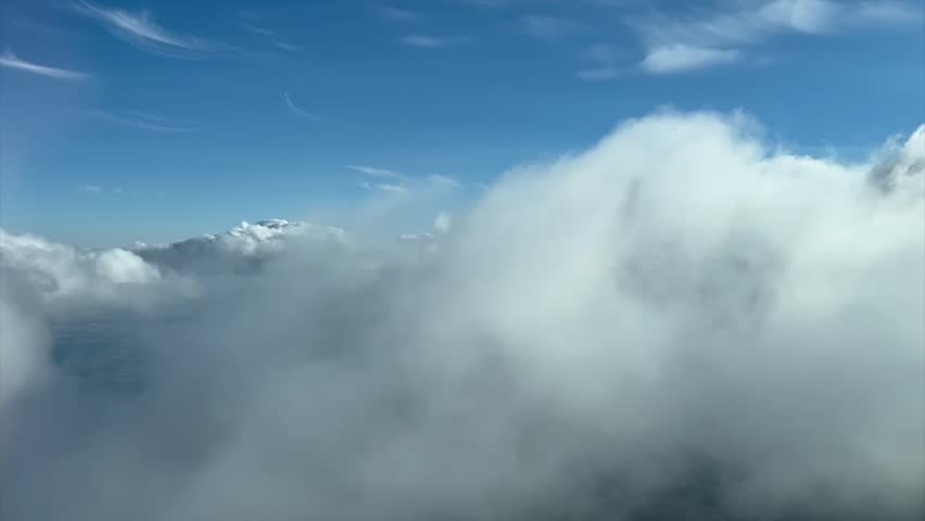 Immersive pilot POV flying through a sunny and blue sky with some white and grey cumulus clouds. Shot from an airplane cockpit. 4K 60FPS