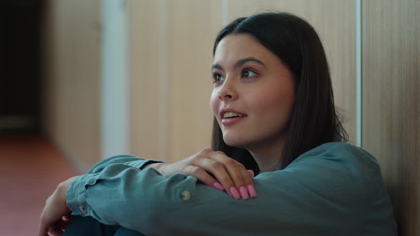 Caucasian happy smiling student girl female schoolgirl woman pupil teen in school university college sitting on floor education study learning waving head yes rhythm move smile dancing listening music