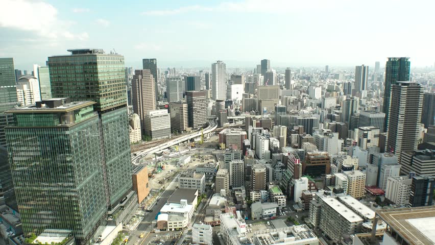 UMEDA, OSAKA, JAPAN - JUNE 2024 : Aerial high angle view around Osaka train station in daytime. View of crowded buildings at downtown area. Urban city and business concept video. Time lapse shot.