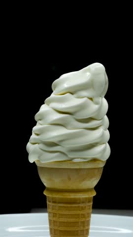 A timelapse vertical footage of a vanilla ice cream melting on a biscuit cone in a white plate then the video reversed with blur black background