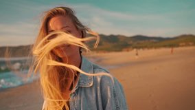 Woman smiling looking camera standing on ocean shore, wind blowing her hair. Portrait shooting happy blonde woman on beach. Young girl in denim shirt enjoying ocean views during sunset. - Powered by Shutterstock - Get 15% off with code: PIKWIZARD15