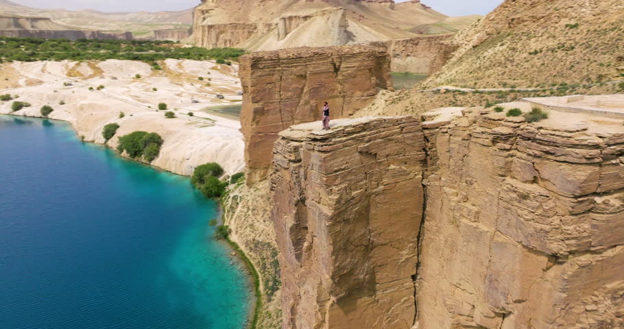 Fearless Man Walks On Top Of Cliff Overviewing Lake At Band-e Amir National Park In Bamyan, Afghanistan. aerial pullback, panning