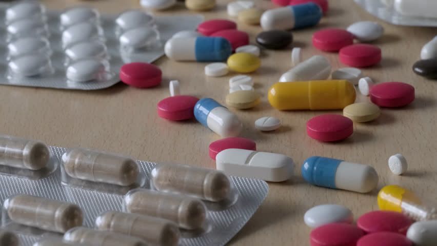 lot of multi-colored pills, capsules, vitamins, drugs, empty blisters on light wooden table, concept maintaining health, pharmaceutical market, medication treatment, deliberate drug overdose