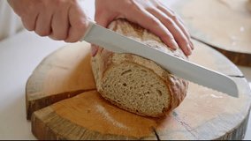 A hand cuts a loaf of bread on a wooden cutting board in a kitchen. - Powered by Shutterstock - Get 15% off with code: PIKWIZARD15