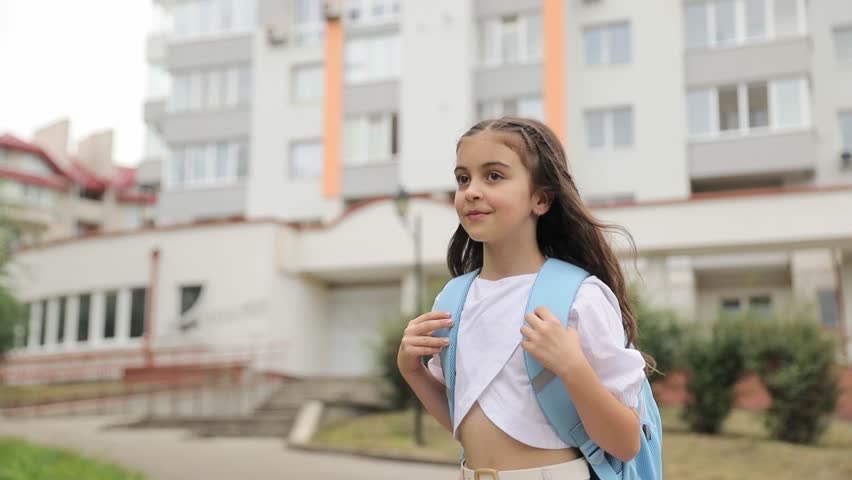 A happy girl with dark hair returns from school walking down a city street