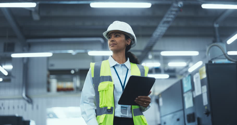 Portrait of a Latin Female Worker in a White Hard Hat Walking Through a Modern, Well-lit Factory, Inspecting Advanced Industrial Machinery, Checking Equipment, Overviewing Production