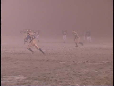 Two (american) football teams face each other an kickoff the ball to start the game on an icy, snowy, fog-bound football field in a Colorado winter