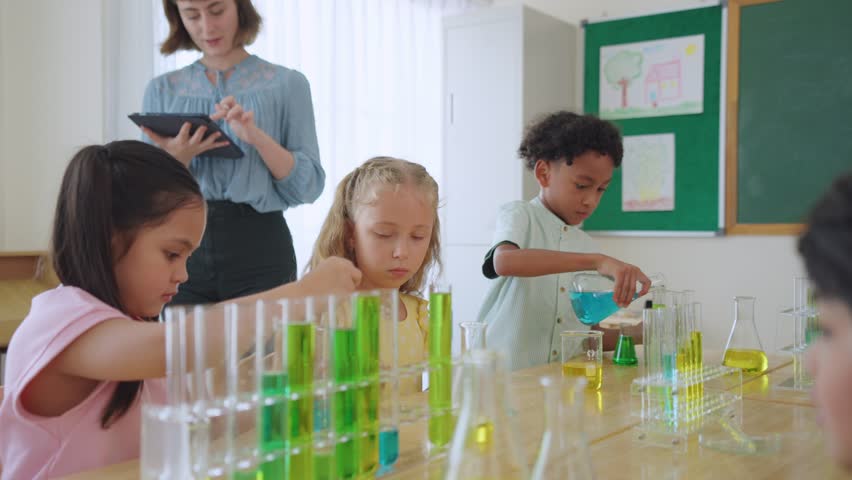 Adorable student learn with teacher in classroom at elementary school. Group of young schoolboy and girl sit on table, study science and doing chemistry experiment with fun activity at kindergarten. - Powered by Shutterstock - Get 15% off with code: PIKWIZARD15