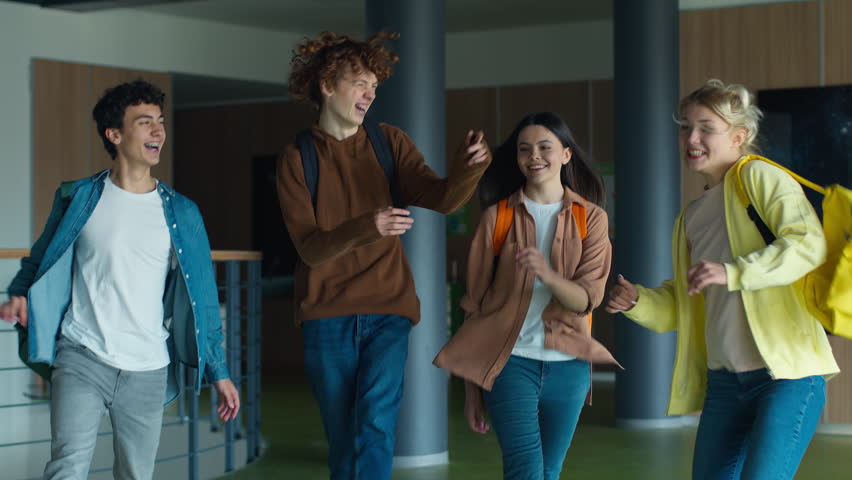 Caucasian students women girls females friends schoolgirls guys boys males men schoolboys walking going jumping dancing in school university college hall corridor happy move celebrate finish lessons