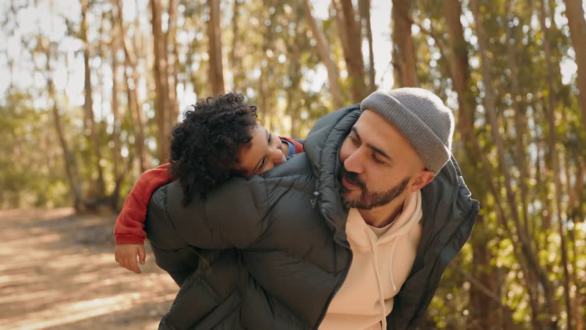 A heartwarming moment captures a smiling father carrying his happy son on his back during a piggyback ride in a serene forest setting.