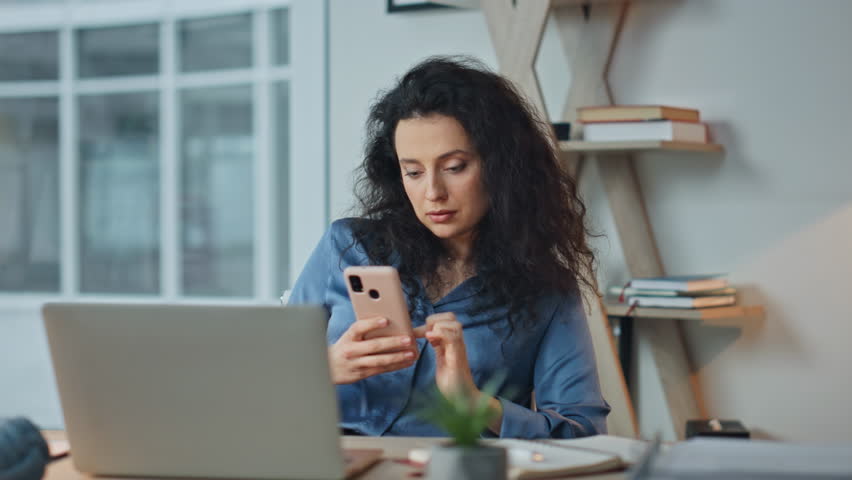 Relaxed businesswoman surfing cellphone in office. Tranquil woman enjoying break resting in chair. Beautiful brunette executive using browsing mobile phone online. Ceo checking messages at workplace