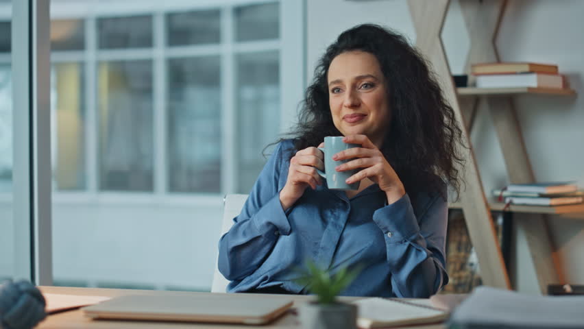 Smiling businesswoman drinking coffee in chair. Closeup relaxed manager resting enjoying tranquil break at agency buro. Beautiful brunette contemplating future success planning project in office.