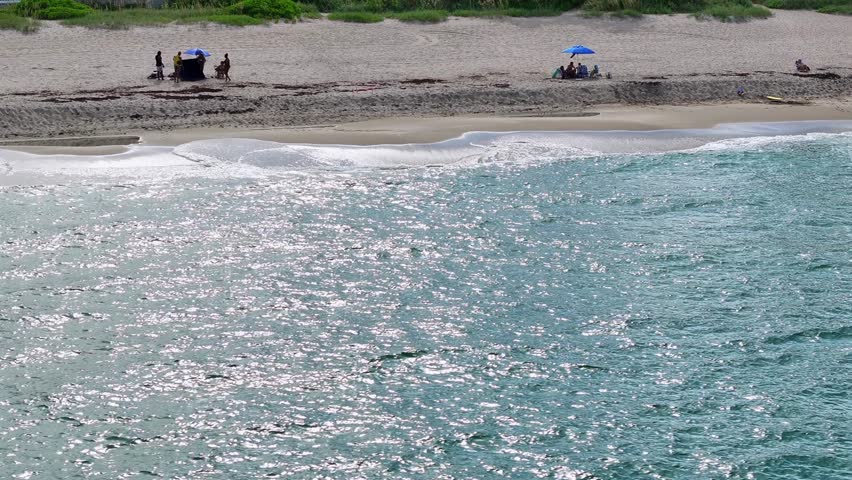 West Palm Beach and Royal Palm Way. Beachgoers with umbrellas, a line of luxury condos and palm trees in the background. Florida coast.
