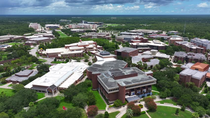 University of Central Florida campus, featuring modern academic buildings, lush green spaces, and expansive walkways, showcasing the university layout. Aerial drone shot.