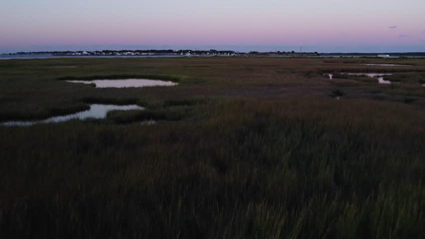 Swamp wetlands with open pools and tall grass reeds and homes on horizon at sunset, Chincoteague Island Virginia, slow motion