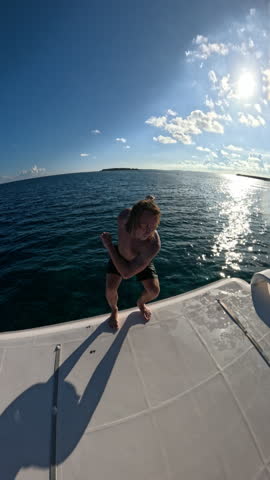 Young man jumps from a boat by flip in salto and dives into the ocean water