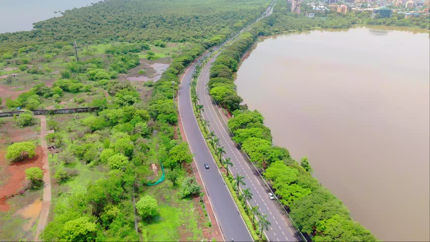 Aerial view of highway between sea and lake, Drone moving up high over city street, Palm beach road navi mumbai, winding expressway, by lush greenery, A large water body on one side, with cityscape