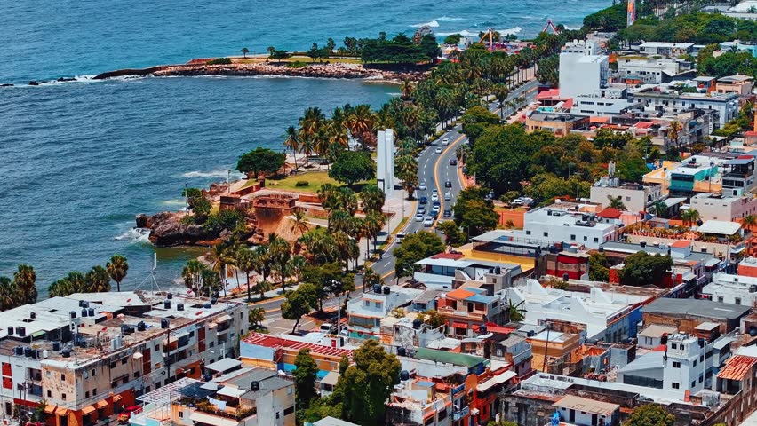 Aerial view of the waterfront of the picturesque seaside city of Santo Domingo. Road on the ocean coast. Panorama of the old city on a sunny day. Drone orbital shot. Beautiful Caribbean landscape.