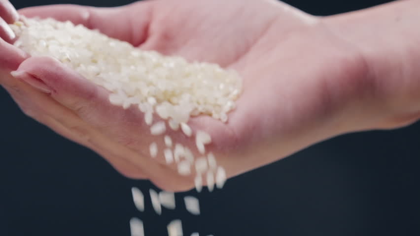 close up on black and blue background there is white round rice on a black long flat plate Japanese culture light protein food A woman's hand pours rice into a plate