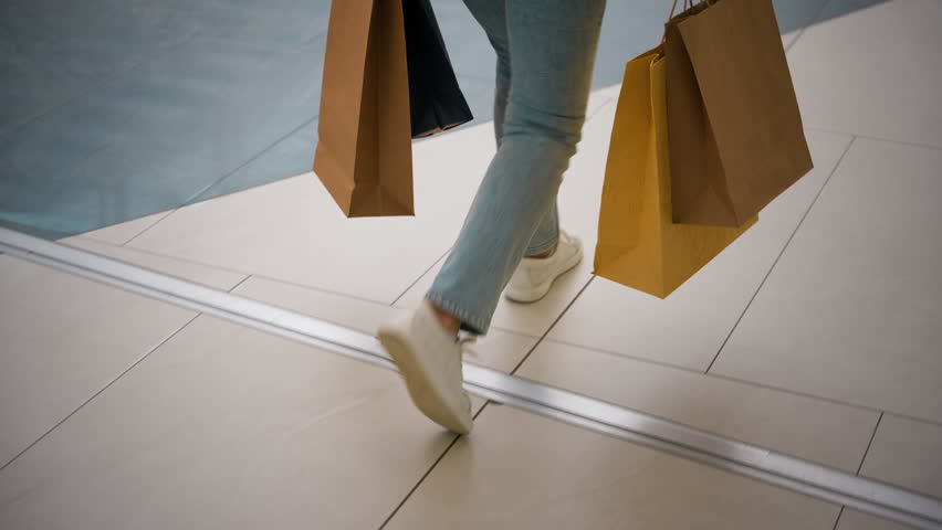 Close up unrecognizable Caucasian woman shopper buyer female legs walking store holding many bags packages. Girl customer purchasing buying clothing gifts Black Friday sales move indoors shopping mall