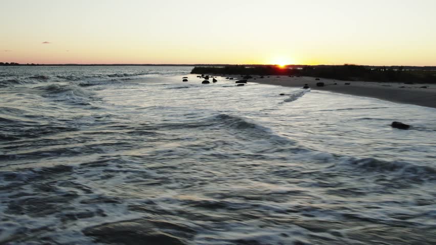 Low aerial orbit rises above ocean waves crashing on shores at sunset, Chincoteague Island Virginia, slow motion